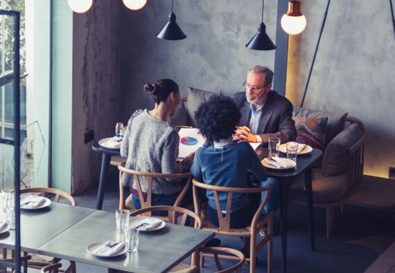 Two female collegues having business meeting in high end restaurant with senior client. Multi-ethnic group. High angle view